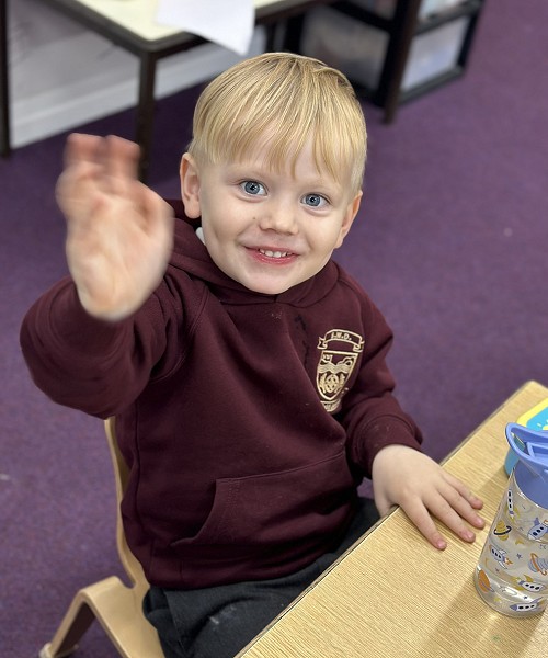 A young boy in school uniform waving