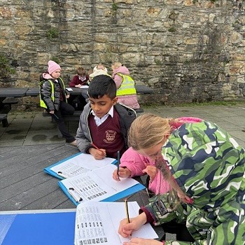 disgyblion yn ysgrifennu ar ddalen y tu allan i furiau'r castell