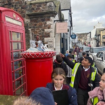 Disgyblion yn mynd heibio i flwch post coch, dyma dop crosio