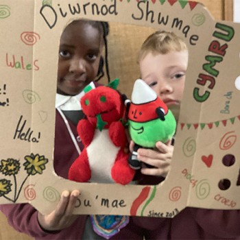 Close view of two children holding a poster alongside Mr Urdd and the Welsh Dragon in the middle