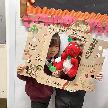 Children holding a poster that says Diwrnod Shwmae with Mr Urdd and the Welsh Dragon in the middle