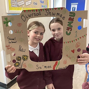Two girls holding Diwrnod Shwmae poster in the classroom