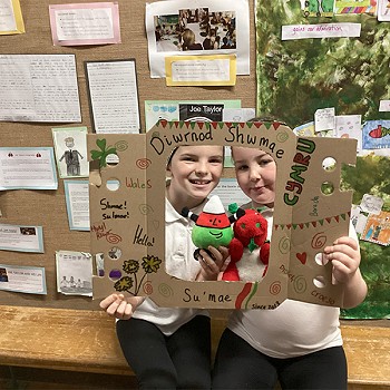 Children holding a poster while holding the Welsh Dragon and Mr Urdd in the classroom